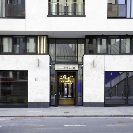 ทาวเวอร์ สวีท บาย บลู ออร์คิด Hotel ลอนดอน ภายนอก รูปภาพ The image shows the entrance of a modern building, characterized by its minimalist architectural design. The facade features a combination of large glass windows and smooth stone surfaces. The entrance is framed by glass doors, flanked by stylish lig