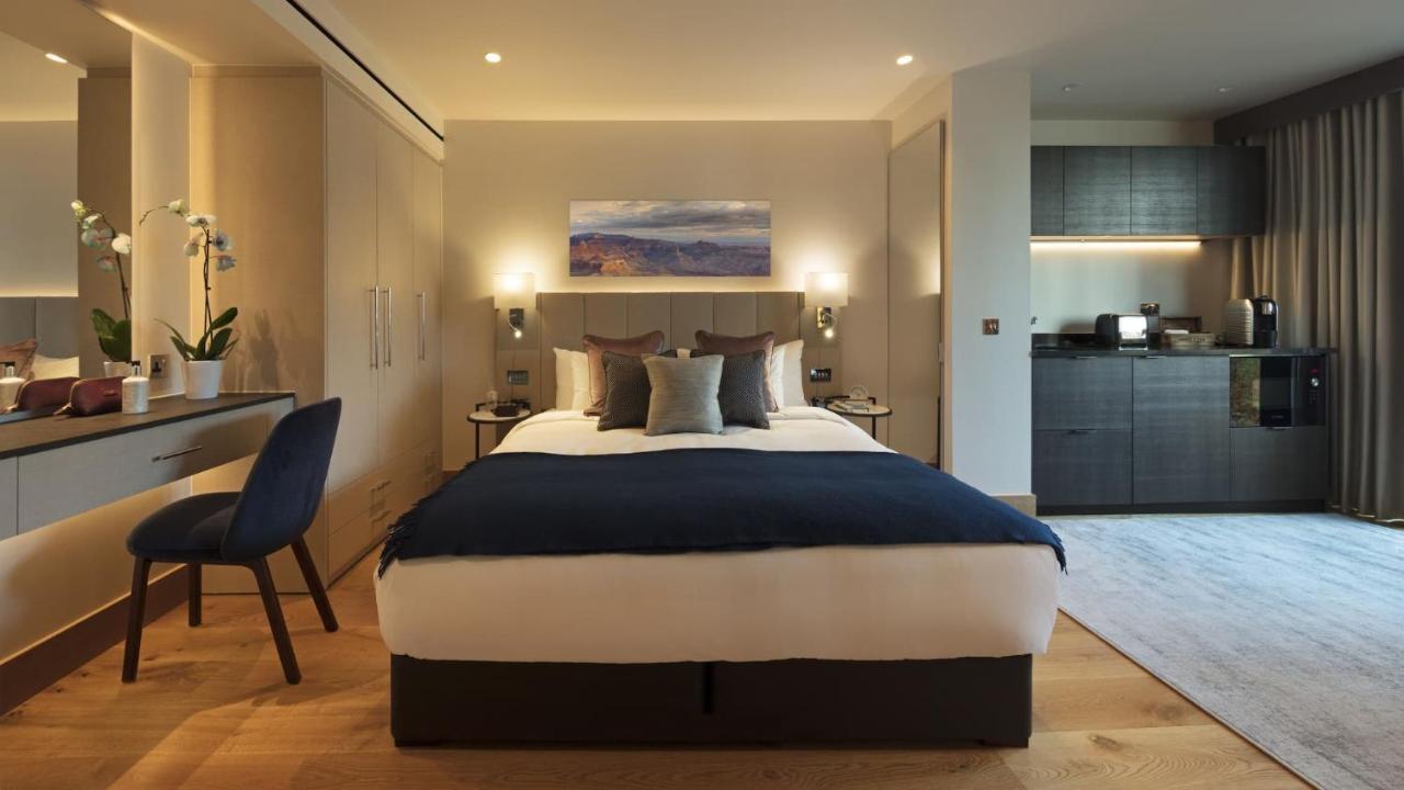 ทาวเวอร์ สวีท บาย บลู ออร์คิด Hotel ลอนดอน ภายนอก รูปภาพ The photo displays a modern hotel room featuring a plush bed with a dark blue bedspread and several decorative pillows. The walls are adorned in neutral tones, and there is a piece of artwork above the bed depicting a serene landscape. On the side, t