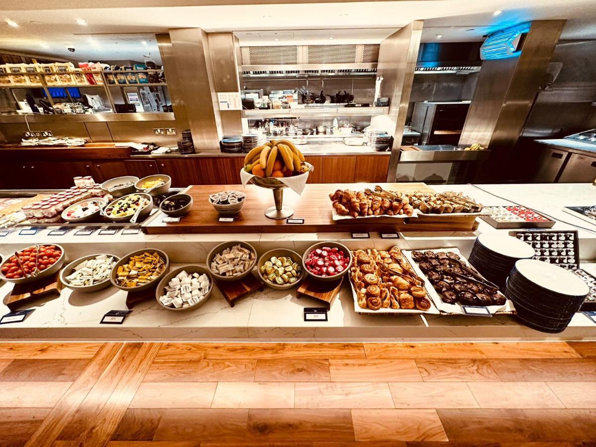 ทาวเวอร์ สวีท บาย บลู ออร์คิด Hotel ลอนดอน ภายนอก รูปภาพ The photo displays a beautifully arranged buffet featuring a variety of food items. There are several bowls and platters filled with colorful fruits, pastries, and desserts. In the center, a large bowl of bananas is prominently placed. Surrounding th