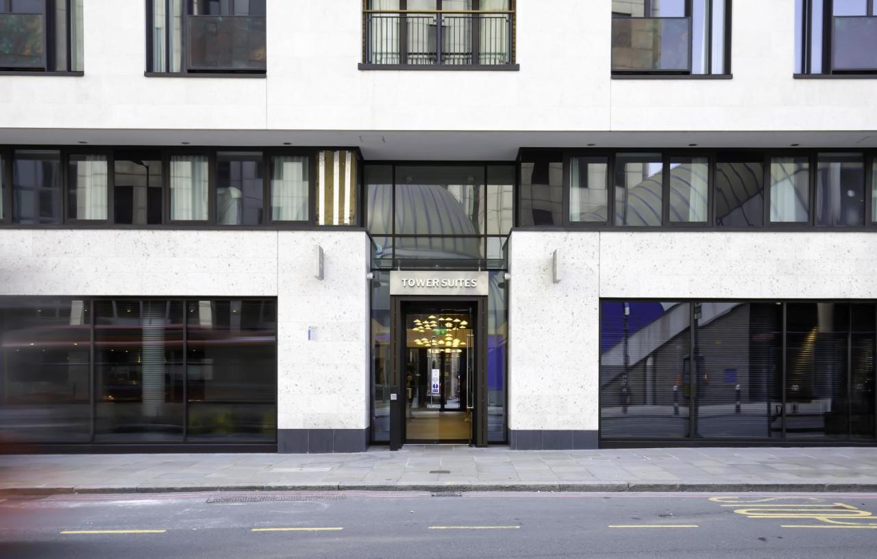 ทาวเวอร์ สวีท บาย บลู ออร์คิด Hotel ลอนดอน ภายนอก รูปภาพ The image shows the entrance of a modern building, characterized by its minimalist architectural design. The facade features a combination of large glass windows and smooth stone surfaces. The entrance is framed by glass doors, flanked by stylish lig