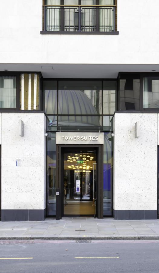 ทาวเวอร์ สวีท บาย บลู ออร์คิด Hotel ลอนดอน ภายนอก รูปภาพ The photo shows the entrance of a building labeled "TOWER SUITES." The entrance features large glass doors, allowing visibility into the interior. The building has a modern architectural style, with a light-colored stone facade and some decorative el
